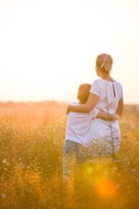 Beautiful young woman with her son on the daisy meadow on a sunny day. Happy family on summer sunset. Kid boy hugging his mother. Happy mum with child.